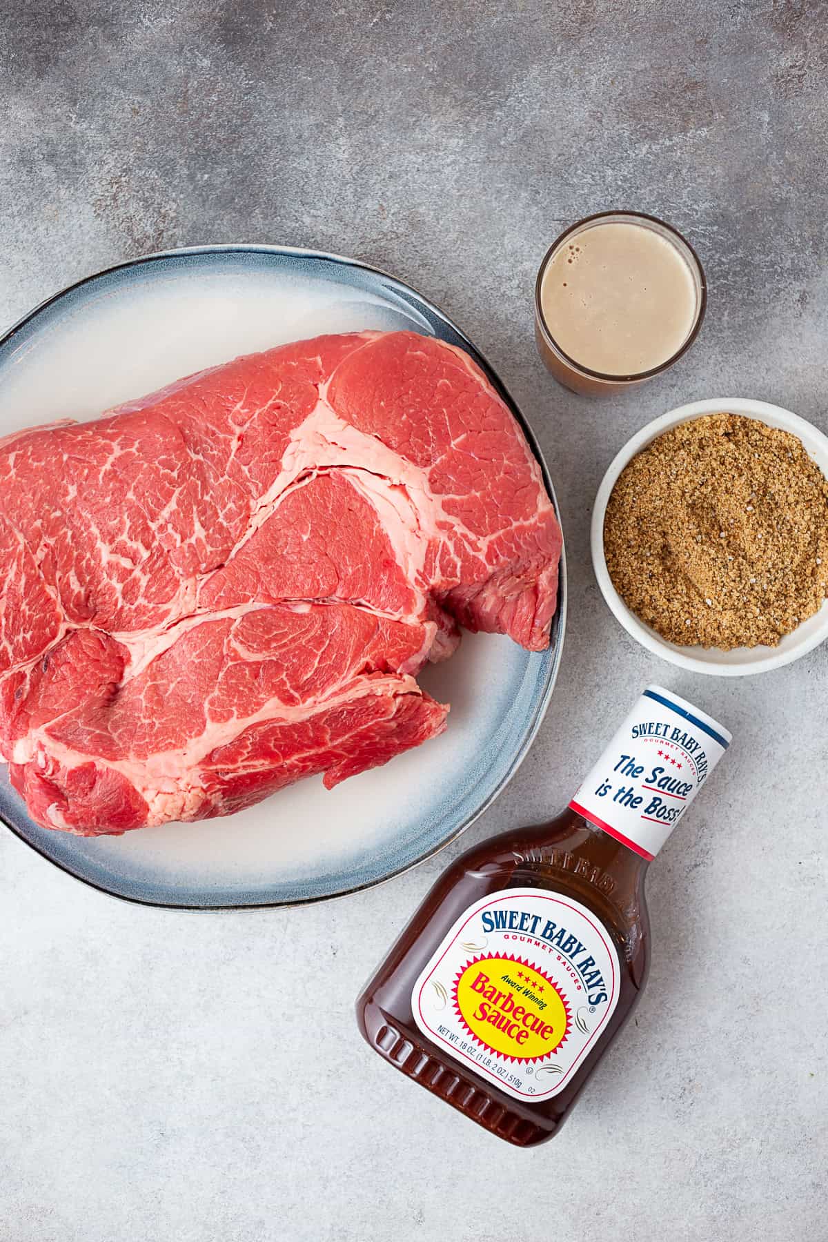 Chuck roast, spices, beef stock, and bbq sauce sitting on a table. 