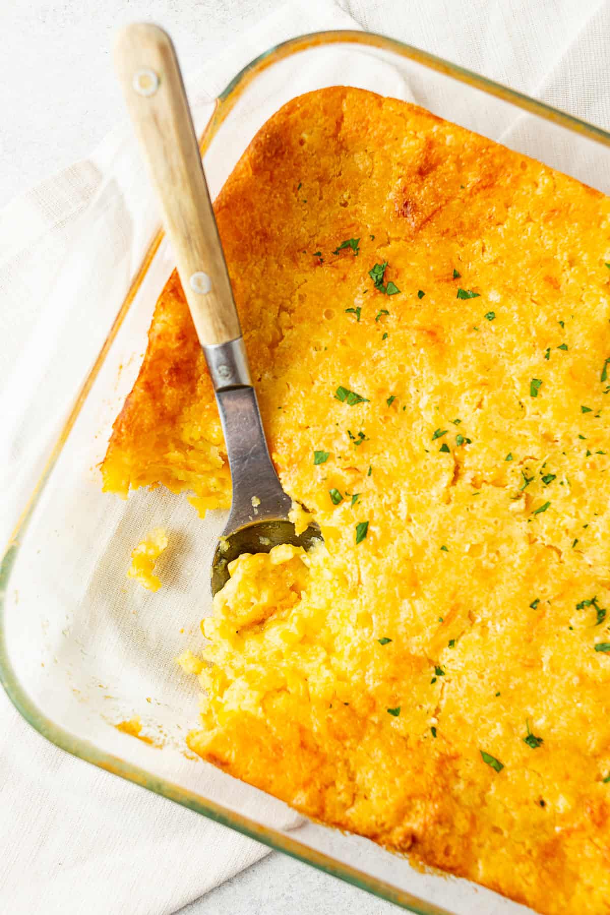 A spoon in a casserole dish of corn souffle. 