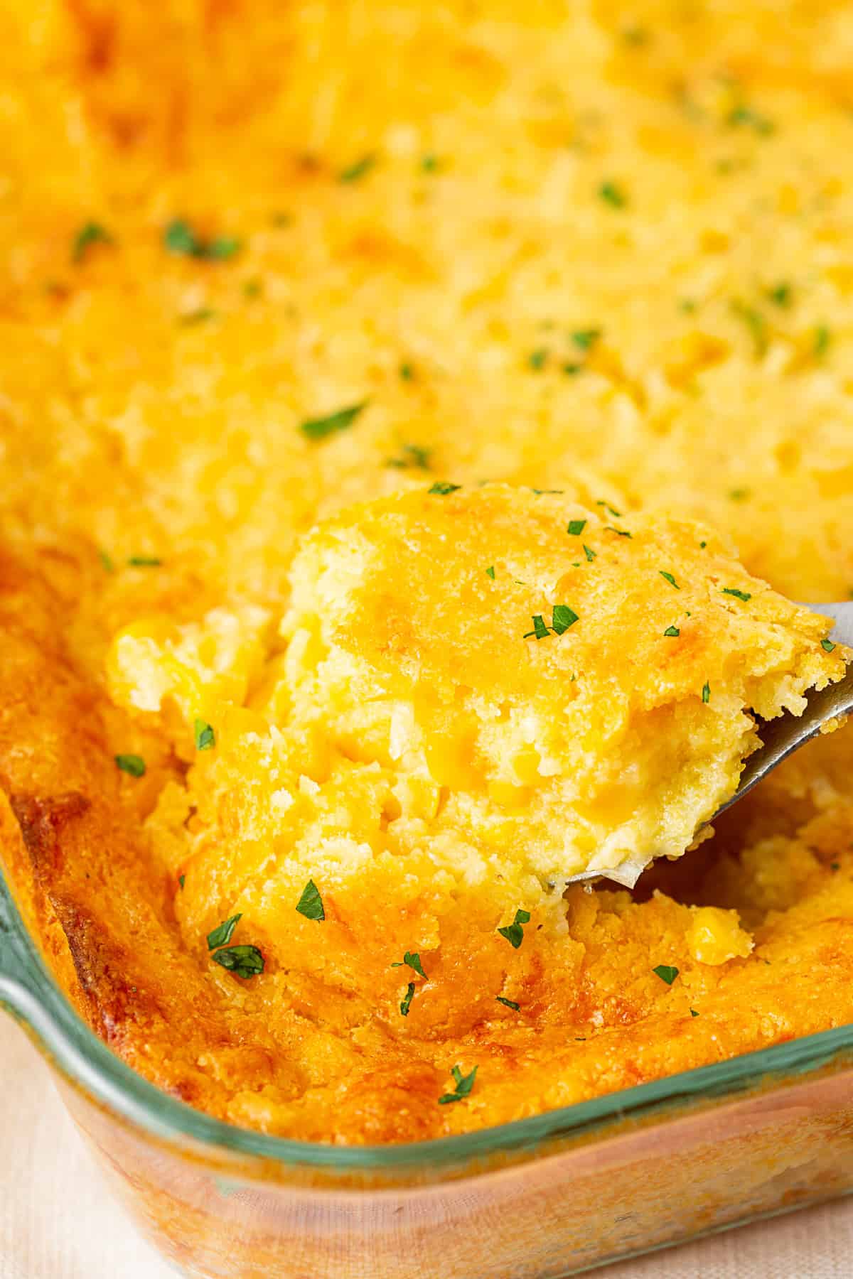 Taking out a scoop of Corn Casserole from a baking dish. 