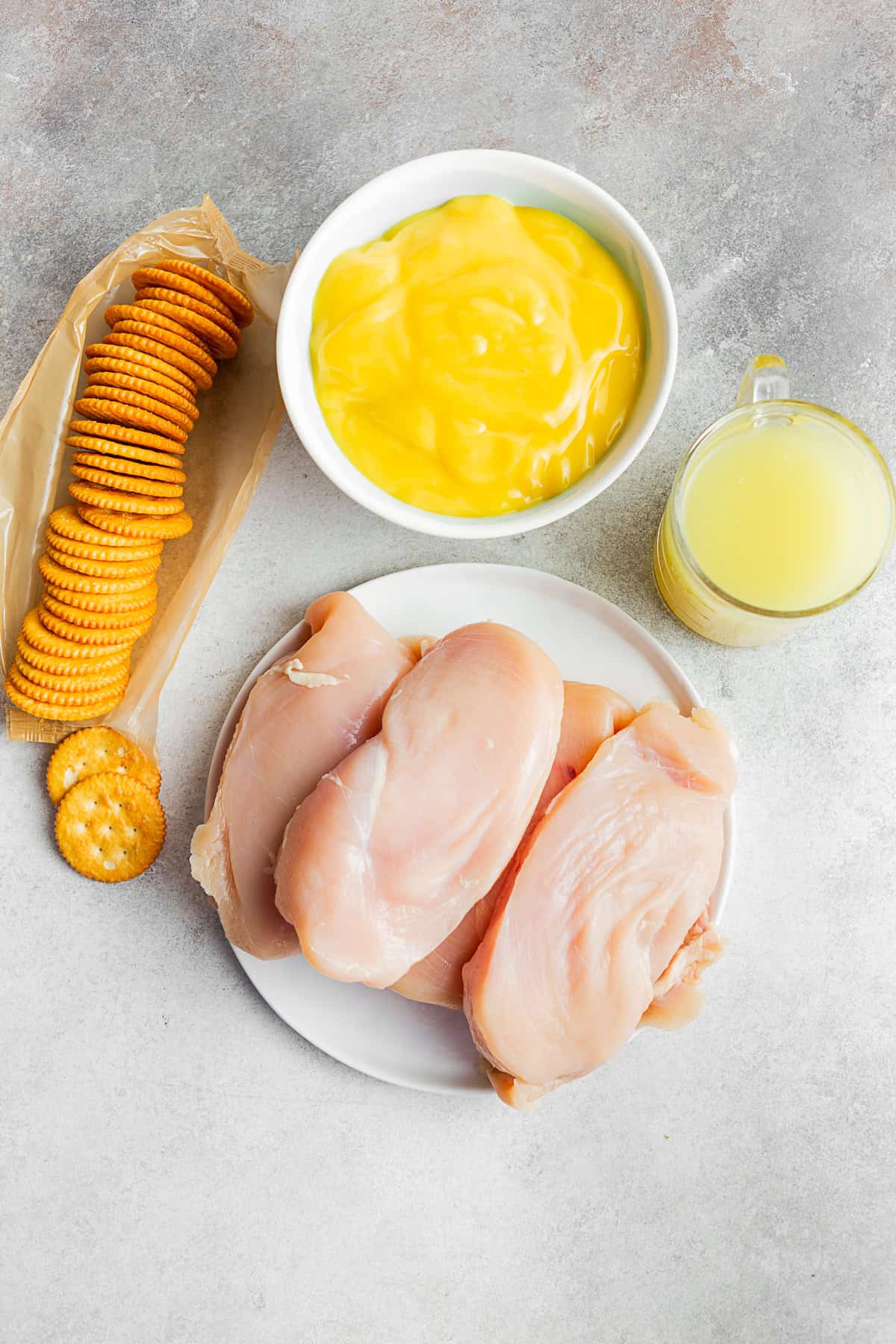 Chicken breast, Ritz crackers, cream of chicken soup, and chicken stock on a table.