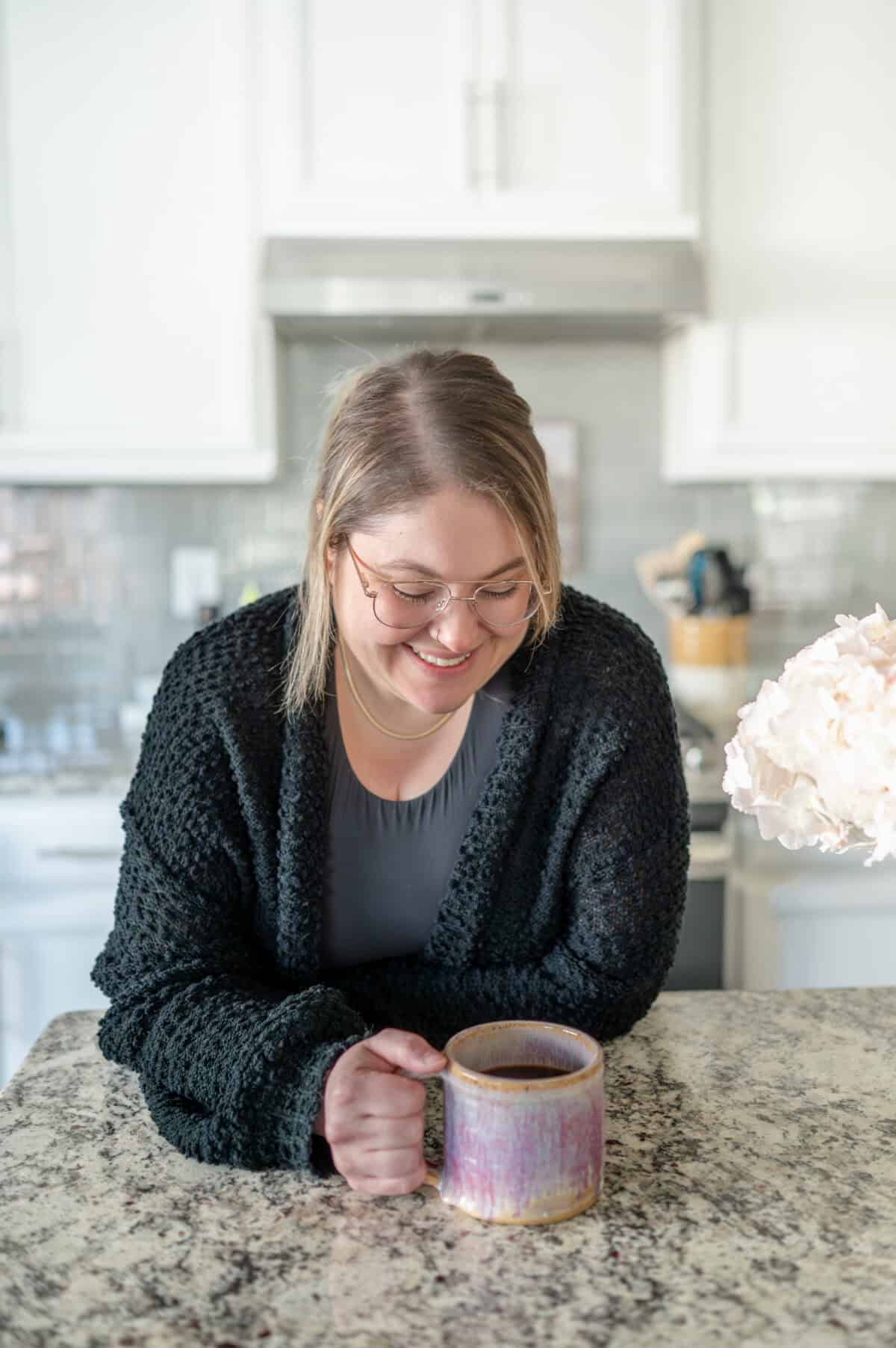 A woman holding a coffee mug in a hand looking down at her coffee.