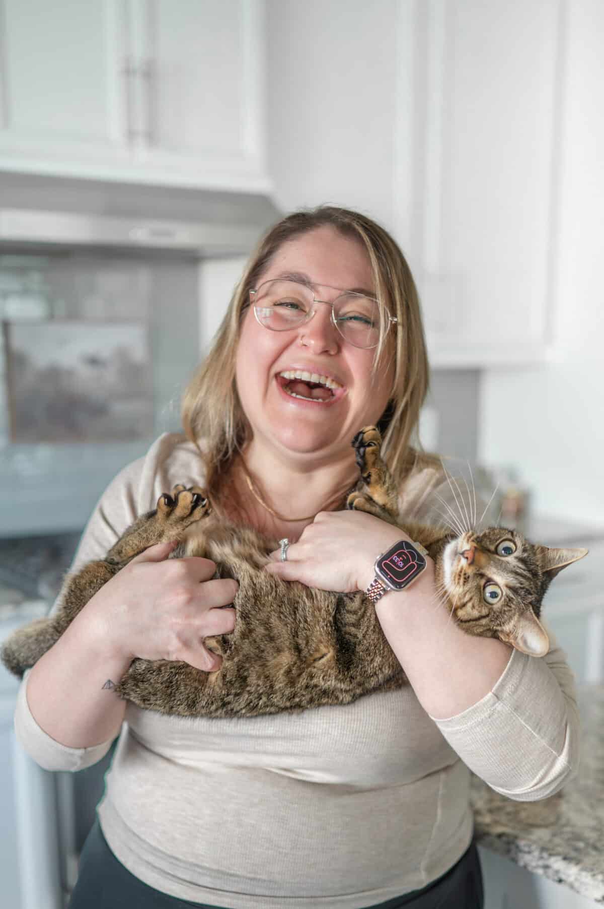A woman laughing while holding her cats in her arms.
