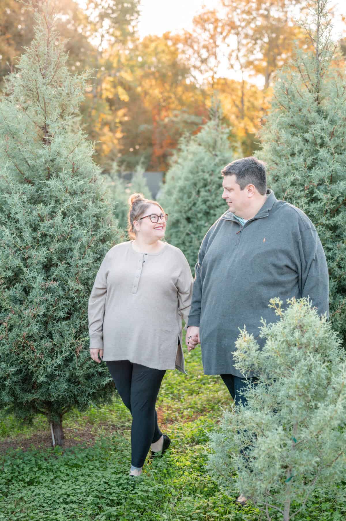 A man and woman walking holding hands in the forest smiling at each other.