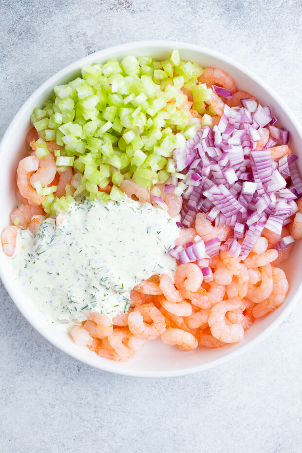 Shrimp, red onion, celery, and salad dressing in a bowl.