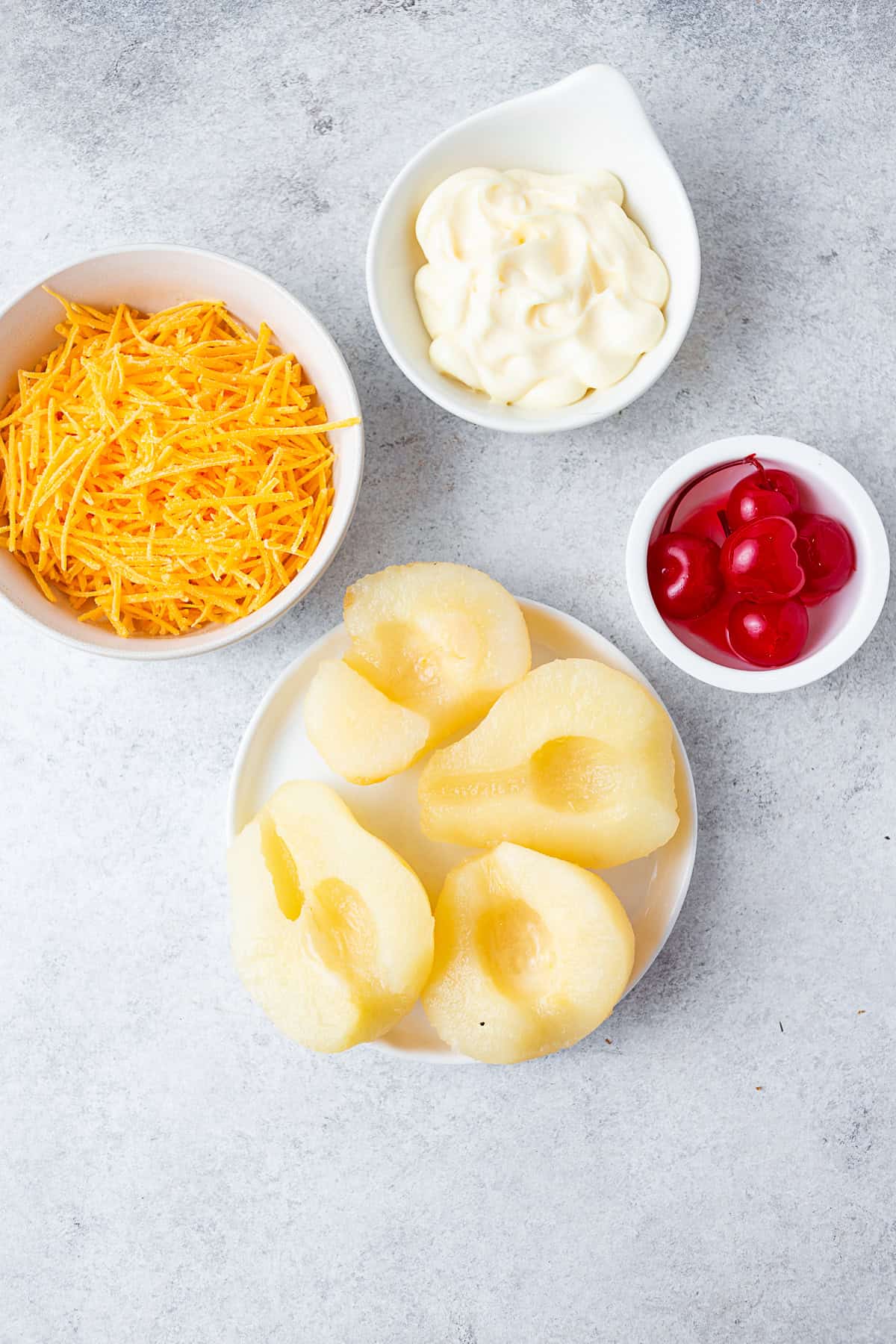 A plate of pear halves, maraschino cherries, mayonnaise, and cheese on a table. 