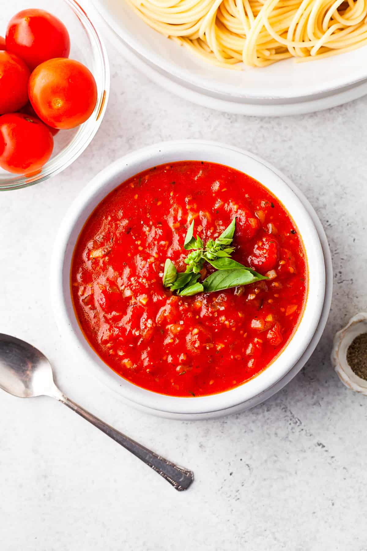 Spicy 30-Minute Tomato Sauce by Nutmeg Nanny Spicy Tomato Sauce in a white bowl with fresh basil sitting on top.