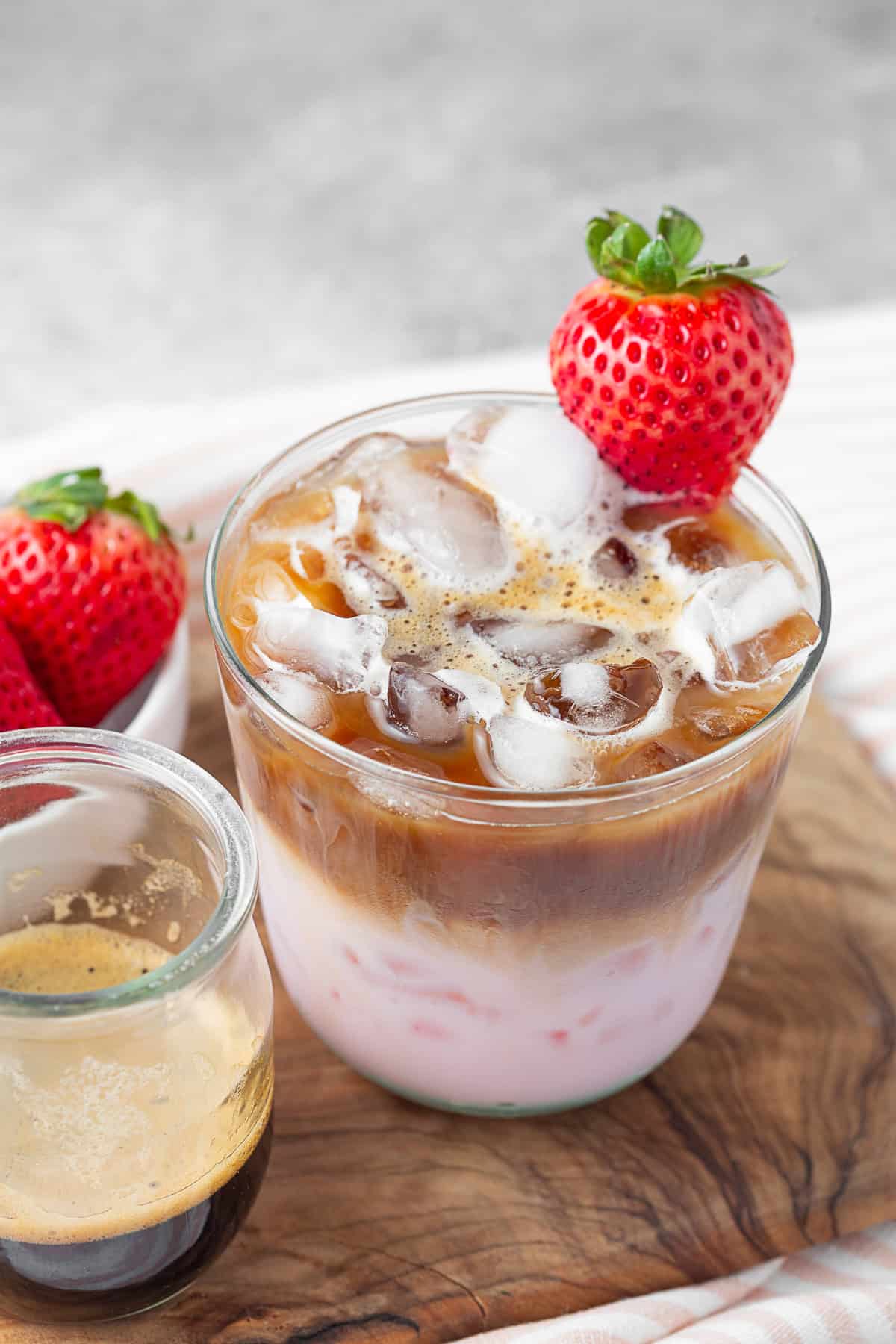 strawberry latte in a small glass with ice and garnished with a strawberry.