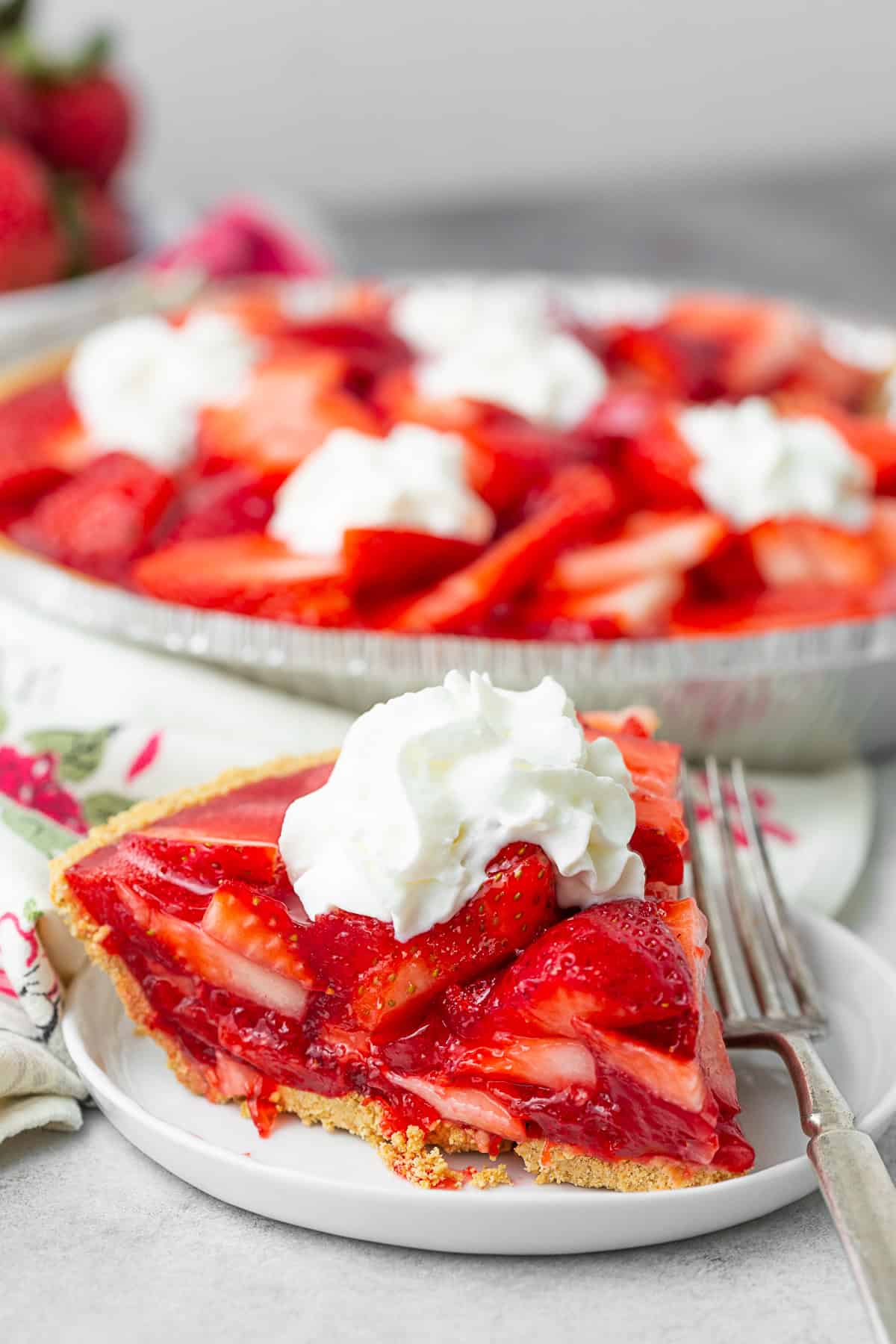 Fresh Strawberry Pie sliced on a plate topped with whipped cream. 