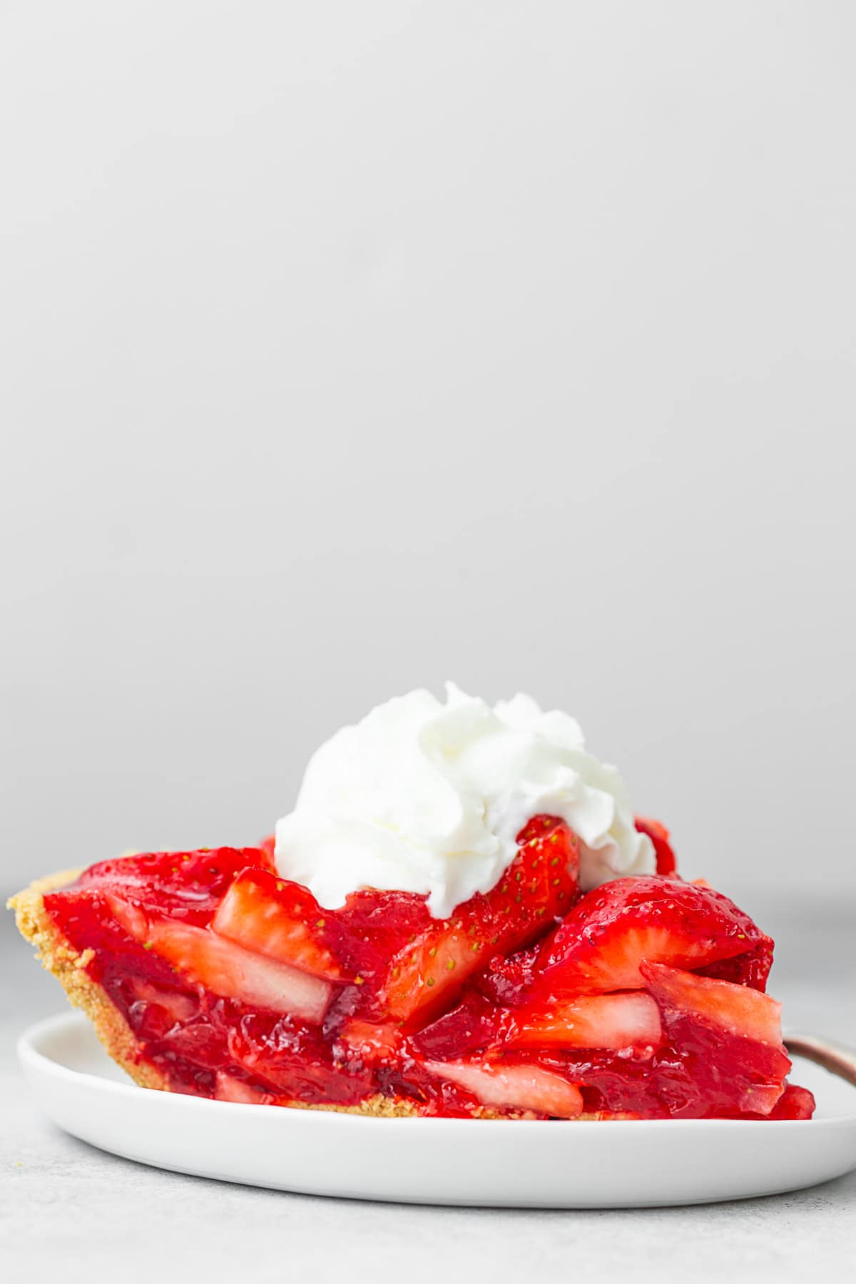 A slice of Fresh Strawberry Pie sitting on a small white plate. 