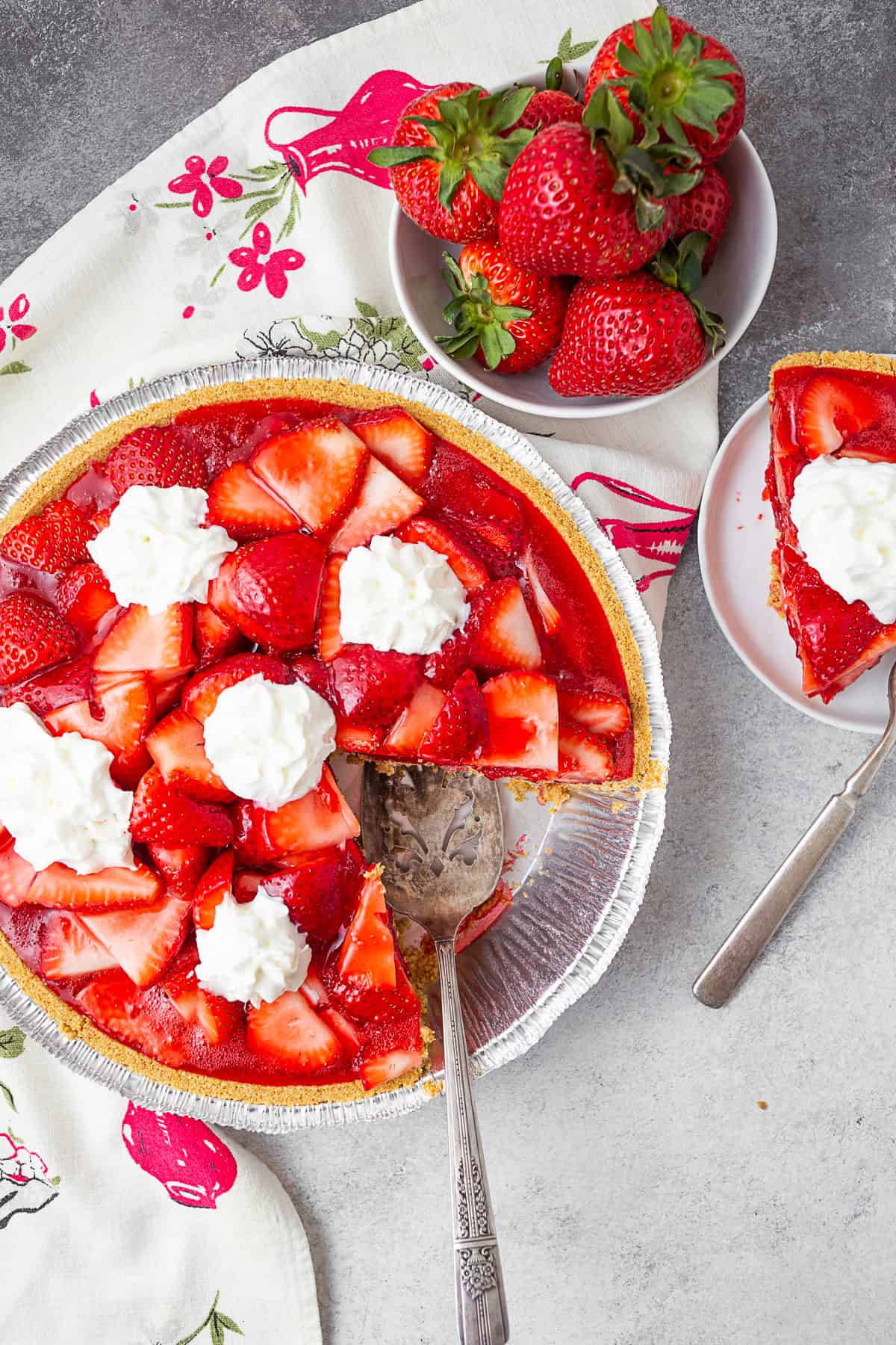 Strawberry pie with a slice on a plate and bowl of berries on a table. 