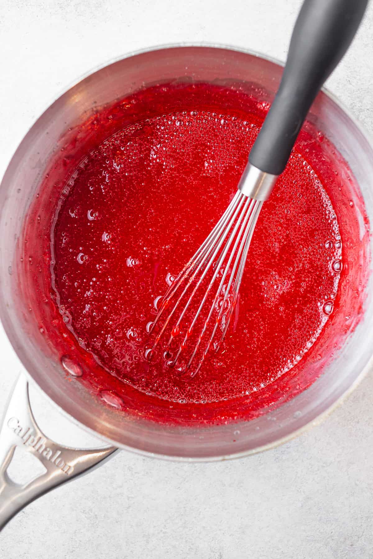 Strawberry gelatin mixture in a saucepot with a whisk. 