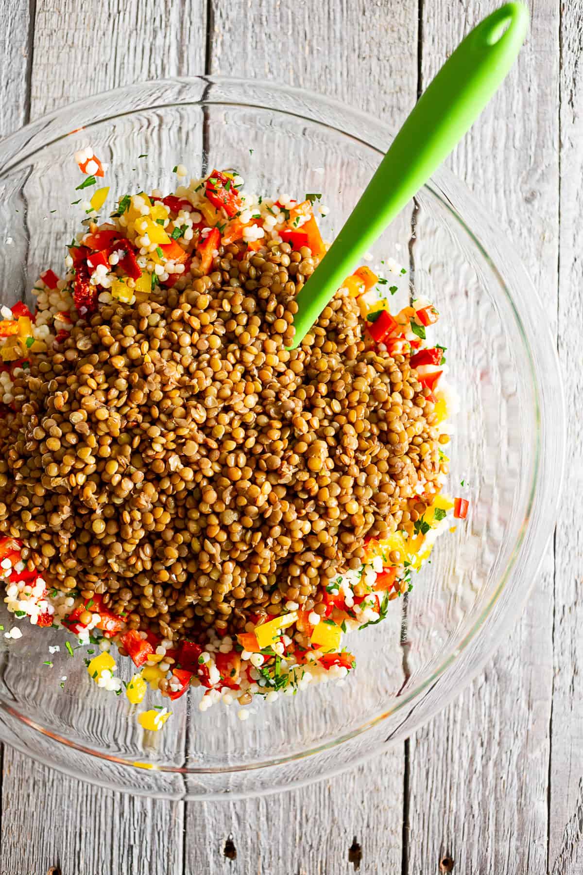 Lentils, couscous and veggies in bowl with a green mixing spoon sticking out.