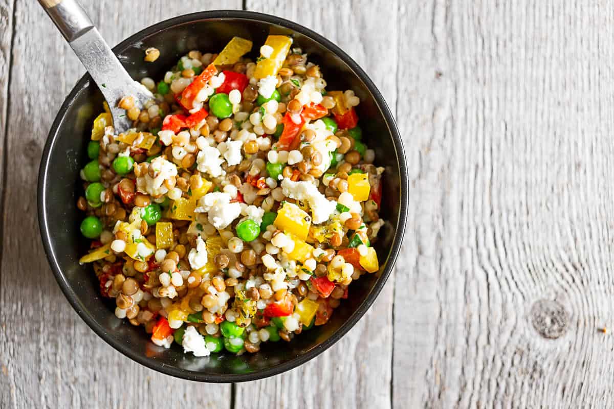 Small black bowl of lentil couscous salad on a gray table with a fork in the bowl.
