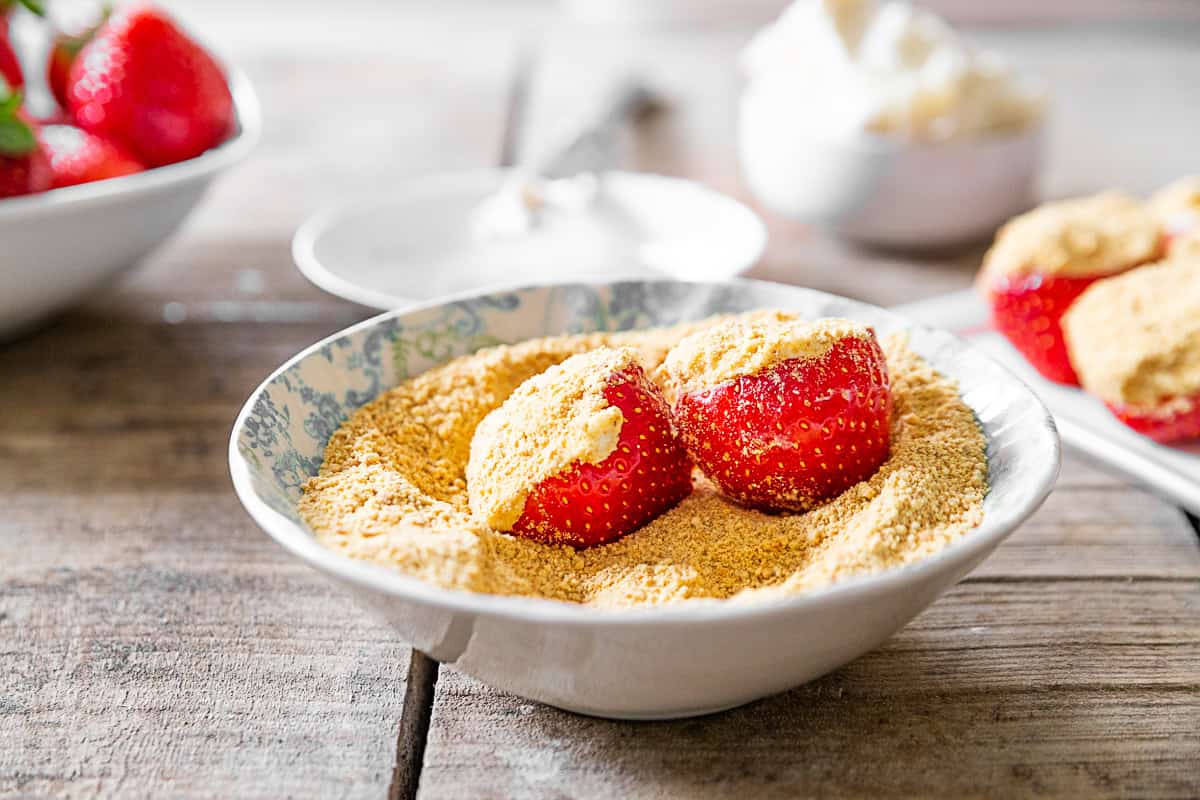 Cheesecake Stuffed Strawberries in a bowl of graham cracker crumbs. 