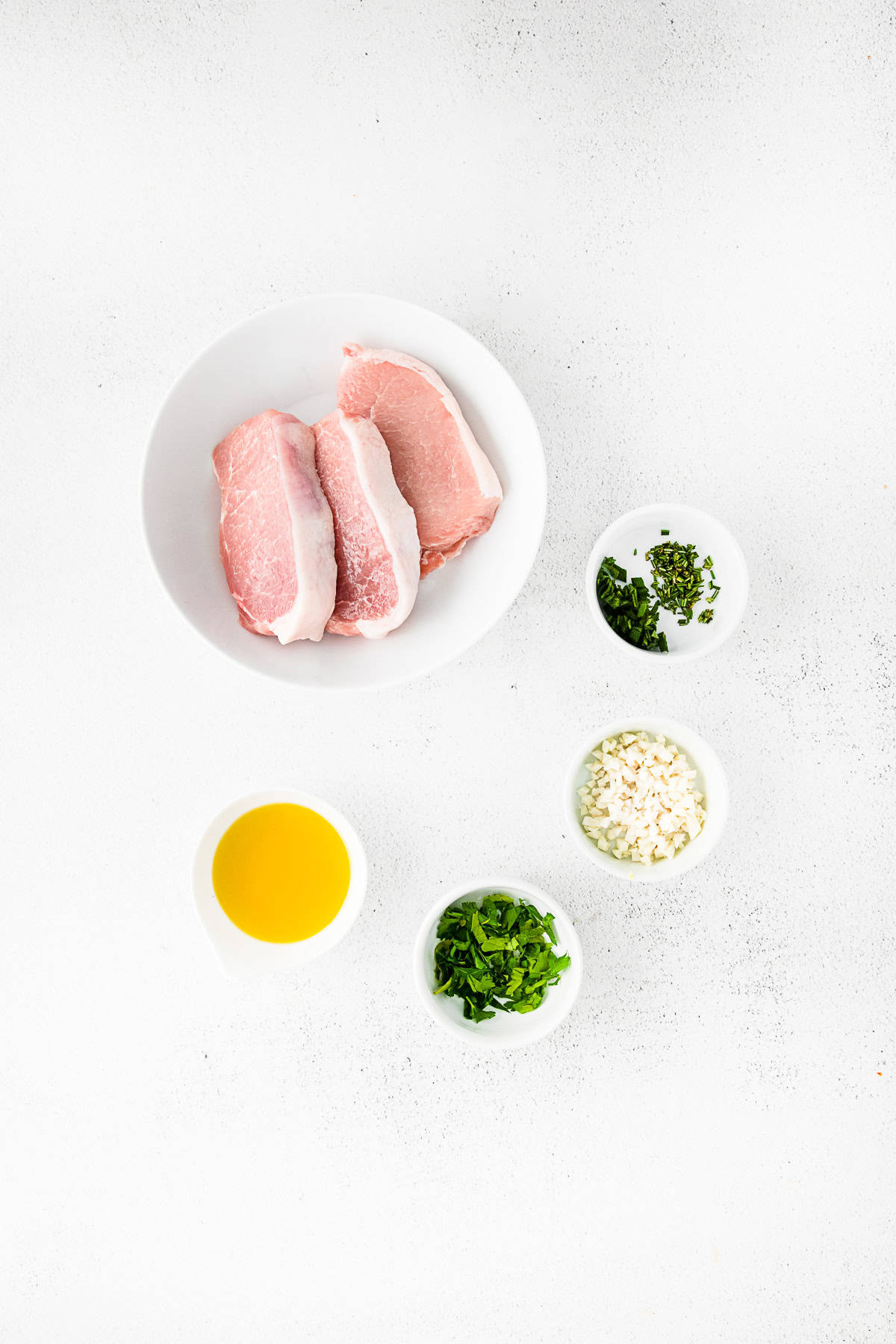 pork chops, olive oil, herbs, and garlic on a table. 