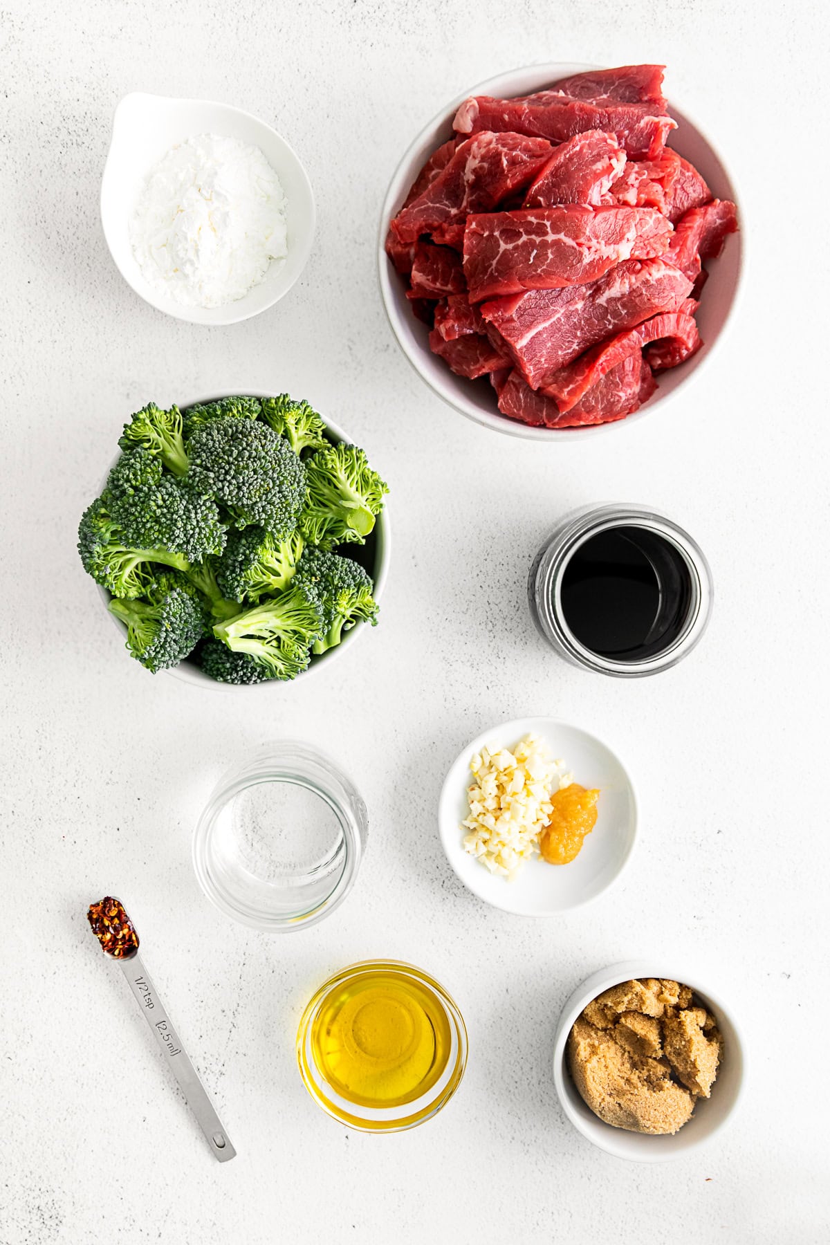 A bowl of beef, broccoli, spices, and herbs on a table. 