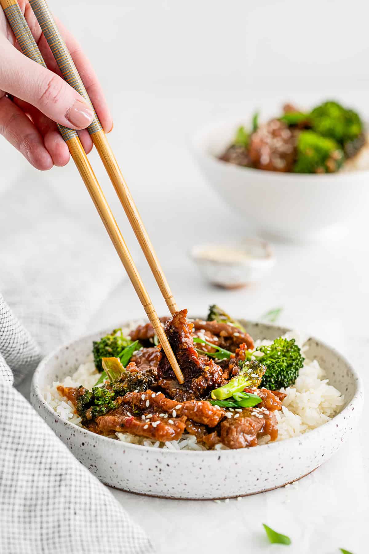 Mongolian beef in a bowl with chopsticks grabbing a piece of meat. 