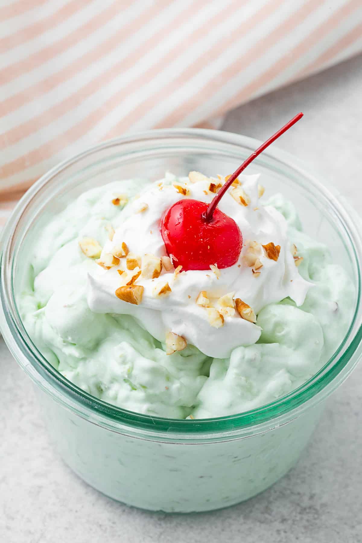 Watergate Salad in a bowl topped with whipped cream, pecans, and a cherry. 
