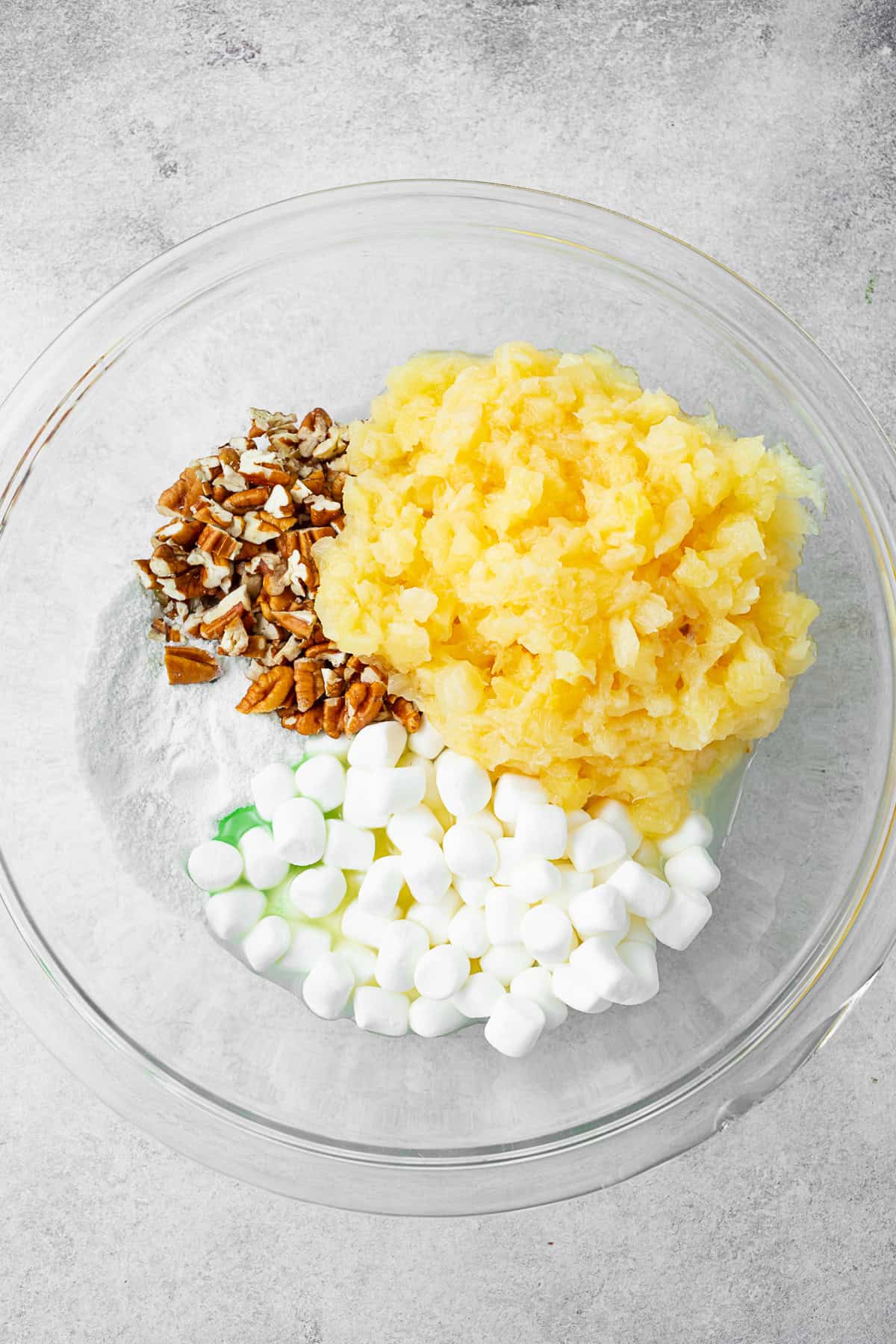 A bowl filled with pineapple, marshmallows, pecans, and pudding mix. 