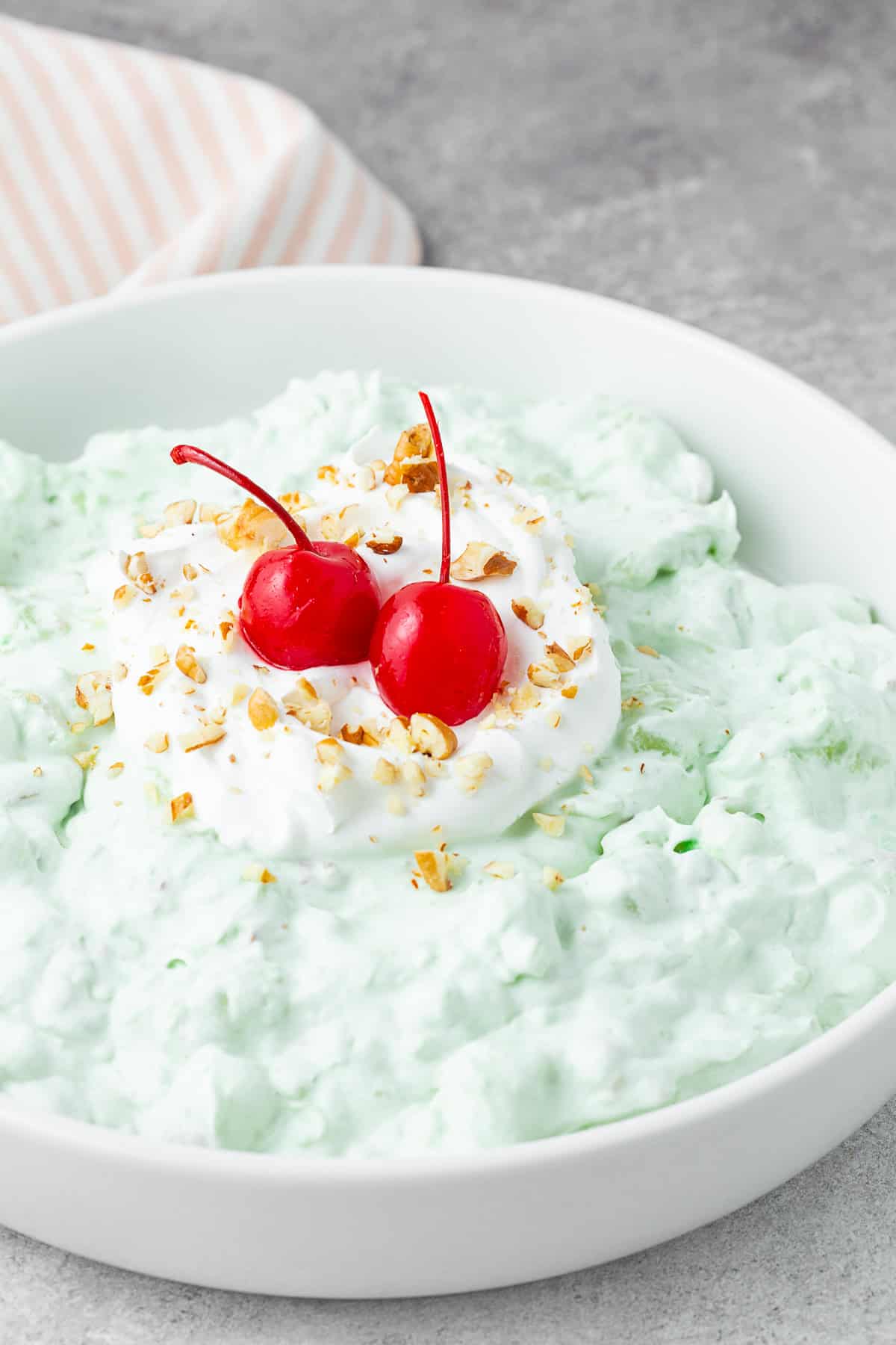 Watergate Salad in a white bowl topped with cherries. 