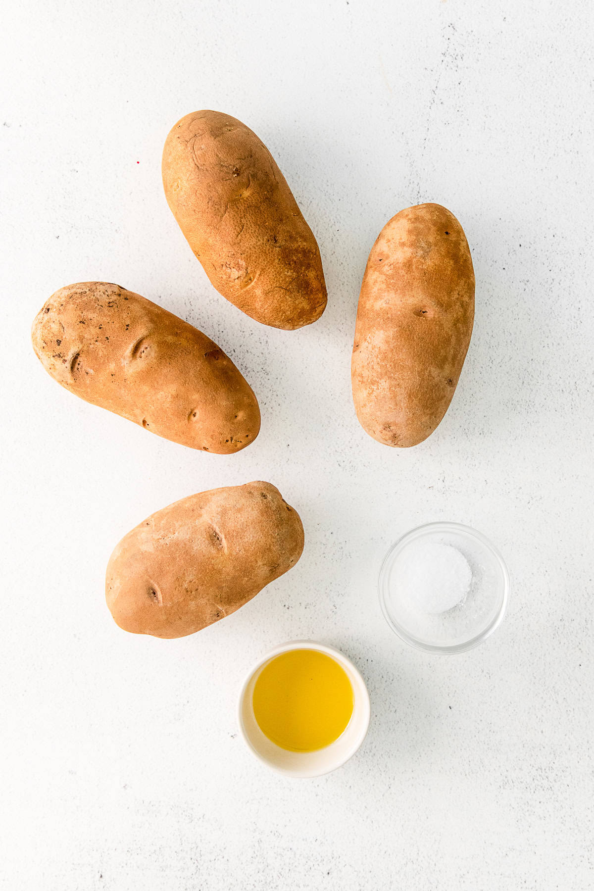 Four potatoes, olive oil, and kosher salt sitting on a table.