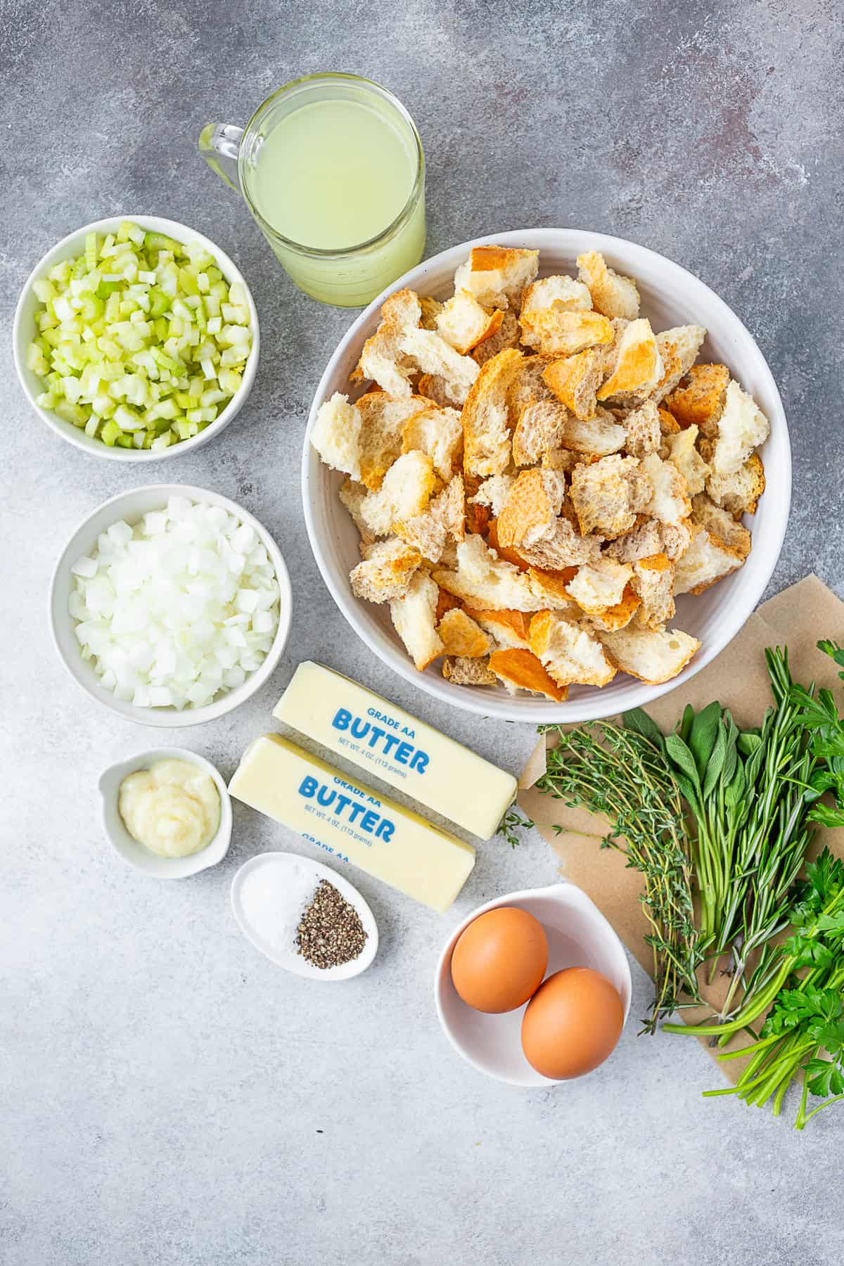 Torn bread, vegetables, butter, eggs, and herbs on a table for stuffing. 