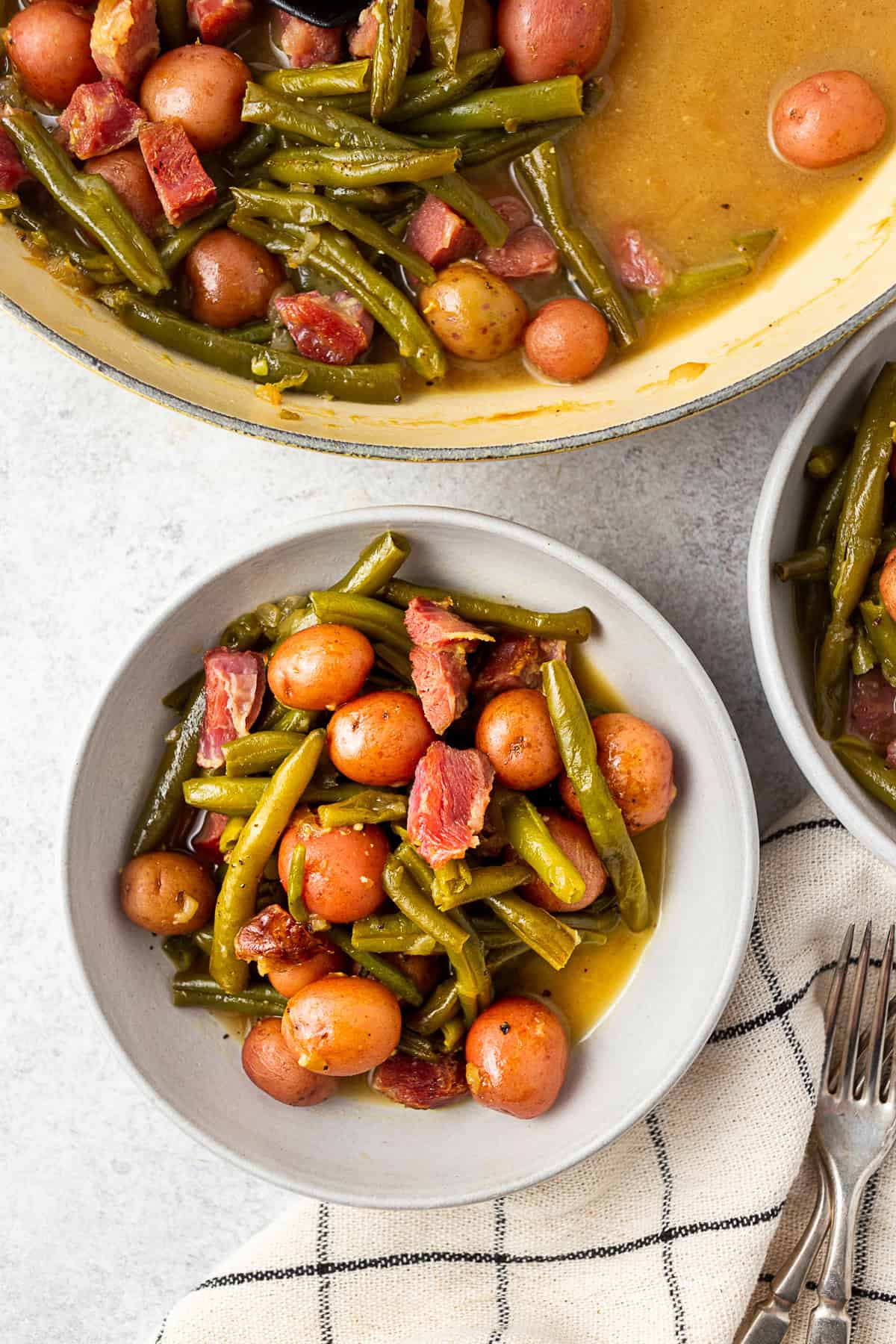 Grey bowl filled with green beans, ham, and potatoes on a table with a napkin.